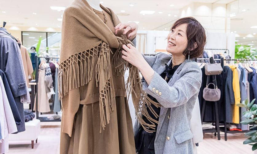 ストアインフルエンサーが店頭のマネキンに着せているブラウンのカーディガンを調整する様子